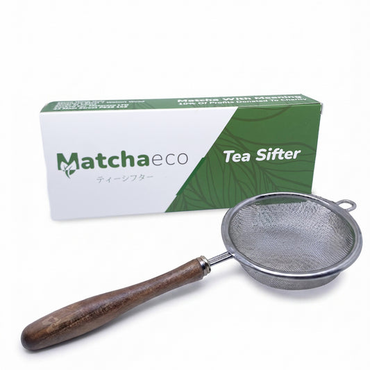A metal tea sifter with a dark brown wooden handle, shown in front of its green and white Matchaeco branded packaging box on a white background.