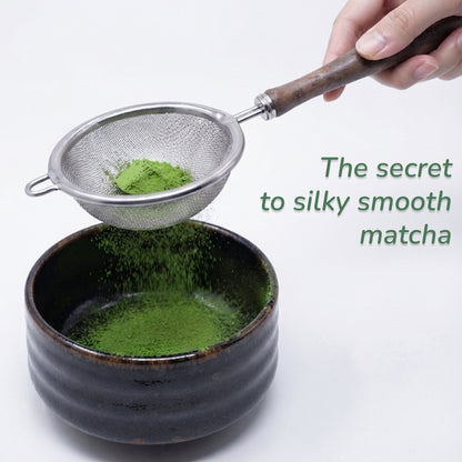 A hand holds a metal matcha sifter over a dark ceramic bowl, pouring bright green matcha powder through the mesh. Text on the right reads, 'The secret to silky smooth matcha.